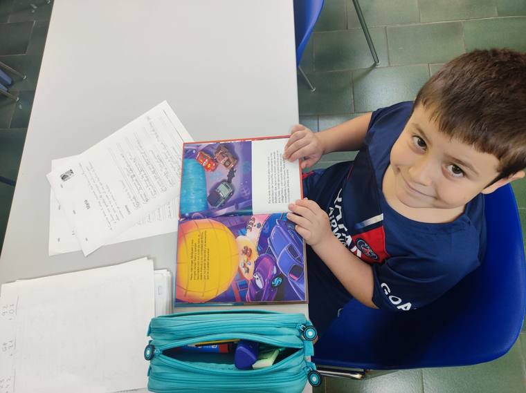 Un alumne somrient amb un llibre i fulls d'exercicis