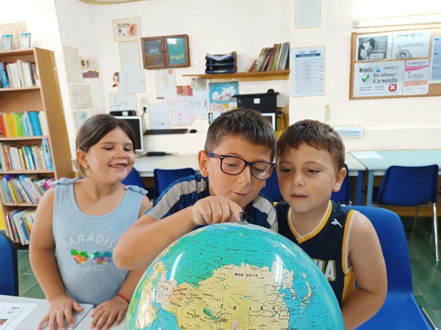 Tres alumnes mirant un globus terraqüi a l'aula